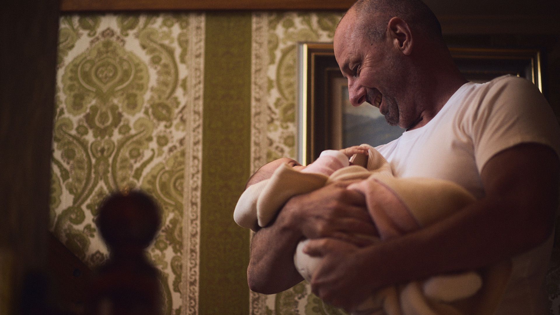 Photo of middle-aged man in a living room, lovingly holding an infant.